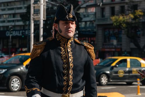Free A man in a traditional military uniform stands on a bustling city street, exuding historical elegance and authority. Stock Photo