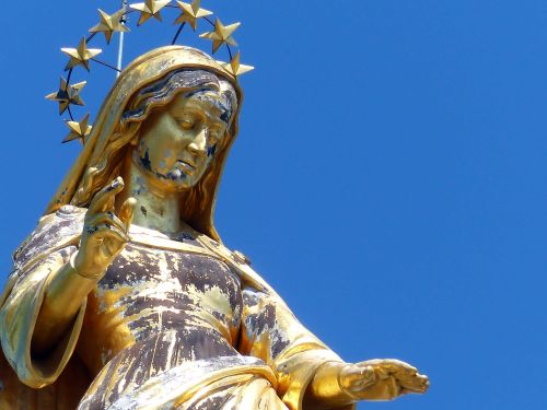 Free Close-up of a gilded Virgin Mary statue with a halo against a clear blue sky. Stock Photo