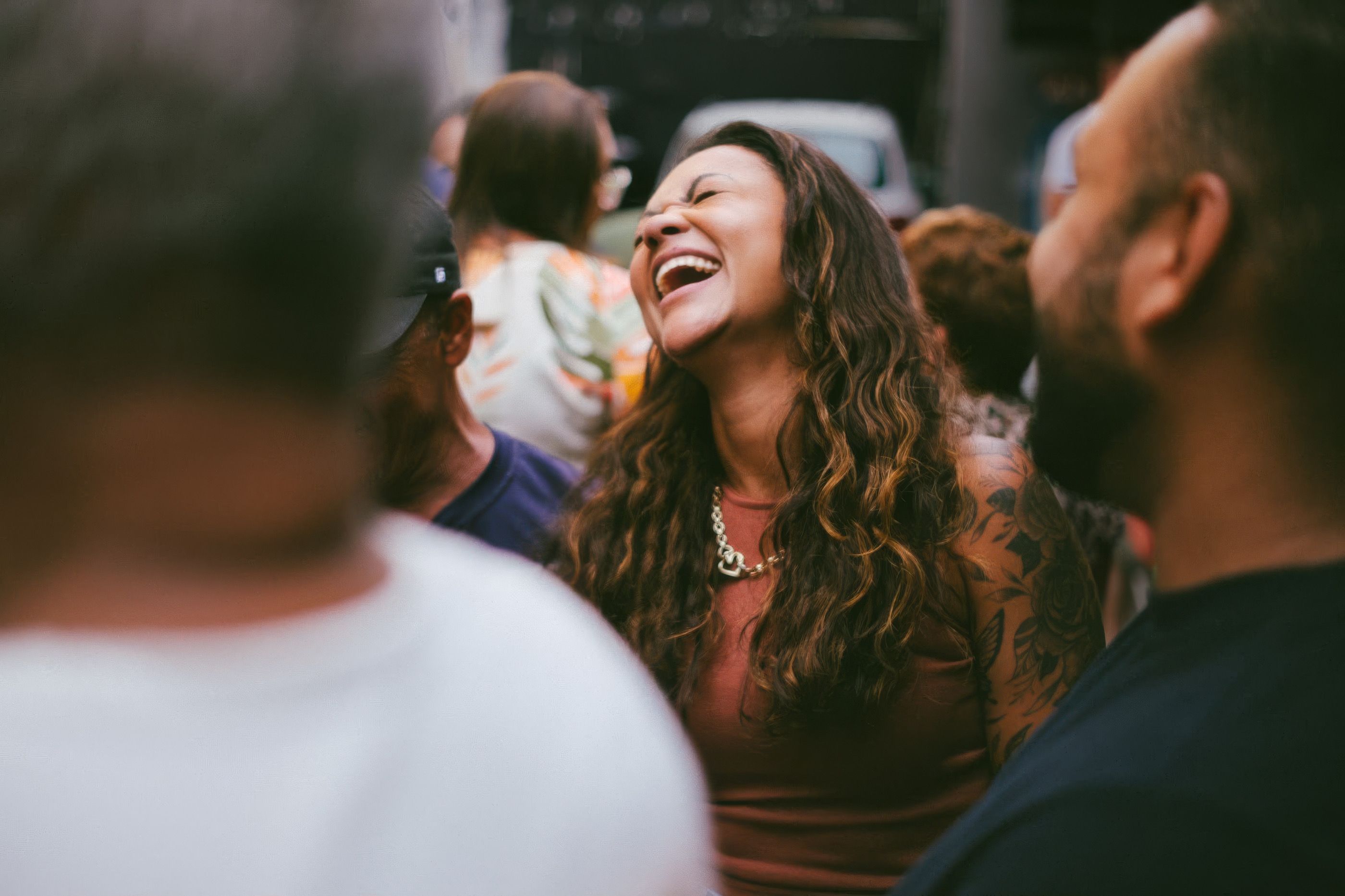 A woman laughing amidst a lively outdoor gathering, capturing joy and connection.