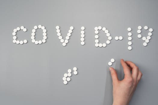 Hand arranging pills spelling 'COVID-19' on a gray background, depicting healthcare theme.