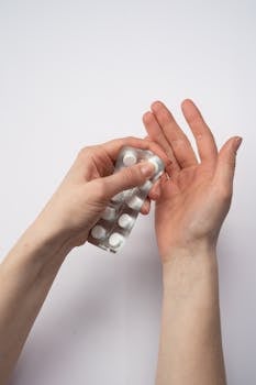 A detailed view of hands holding a blister pack of white pills, isolated on a white background.