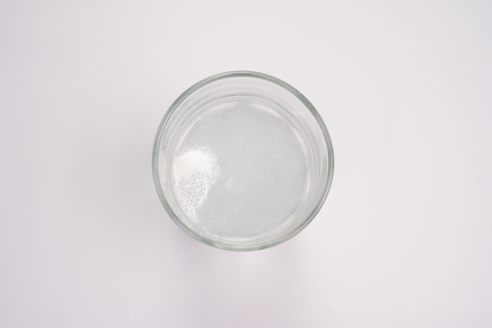 Top-down view of an effervescent tablet dissolving in a glass of water, creating bubbles.