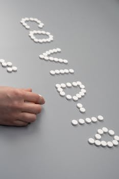 White pills arranged to spell 'COVID' on a gray table with a hand arranging them, symbolizing healthcare efforts.