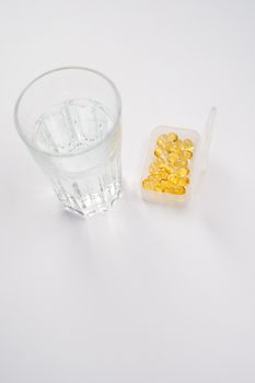 干净的白色表面放着一杯水，旁边是一个装有鱼油胶囊的容器