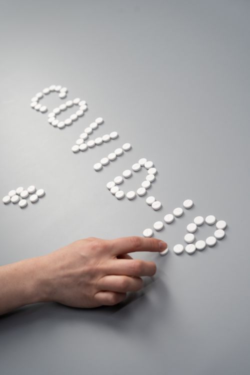 Free Hand arranging white tablets to spell COVID-19, emphasizing pandemic and healthcare themes. Stock Photo