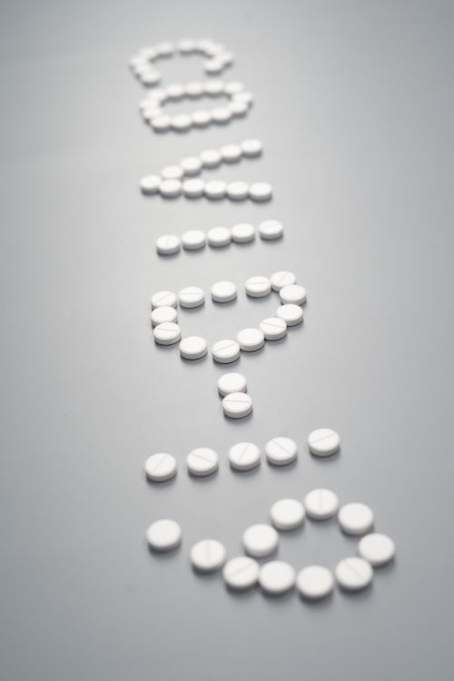 Free White pills artistically arranged to form the text SOS, symbolizing a call for help or medical emergency. Stock Photo