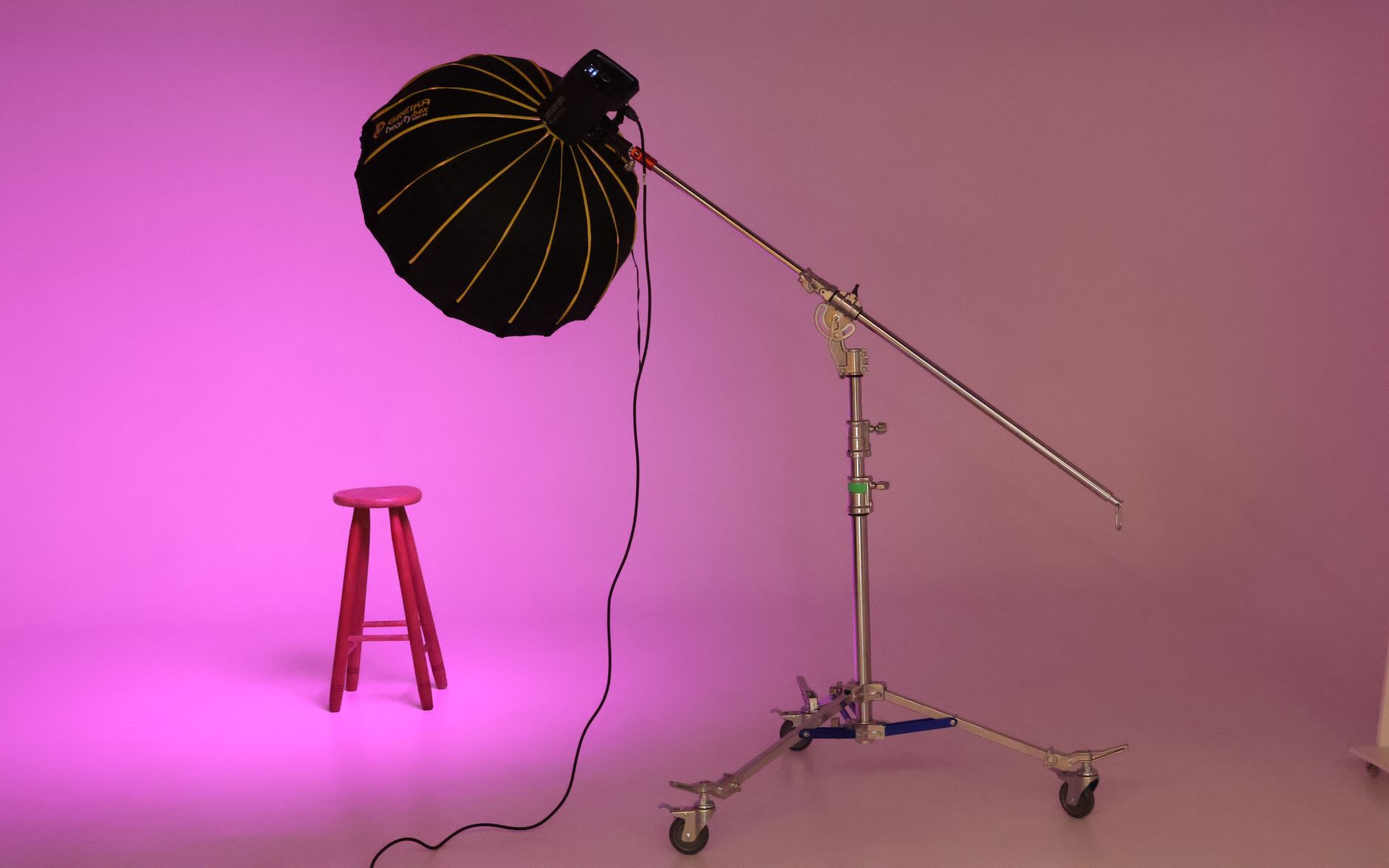 Studio lighting setup with softbox and stool against a pink backdrop.