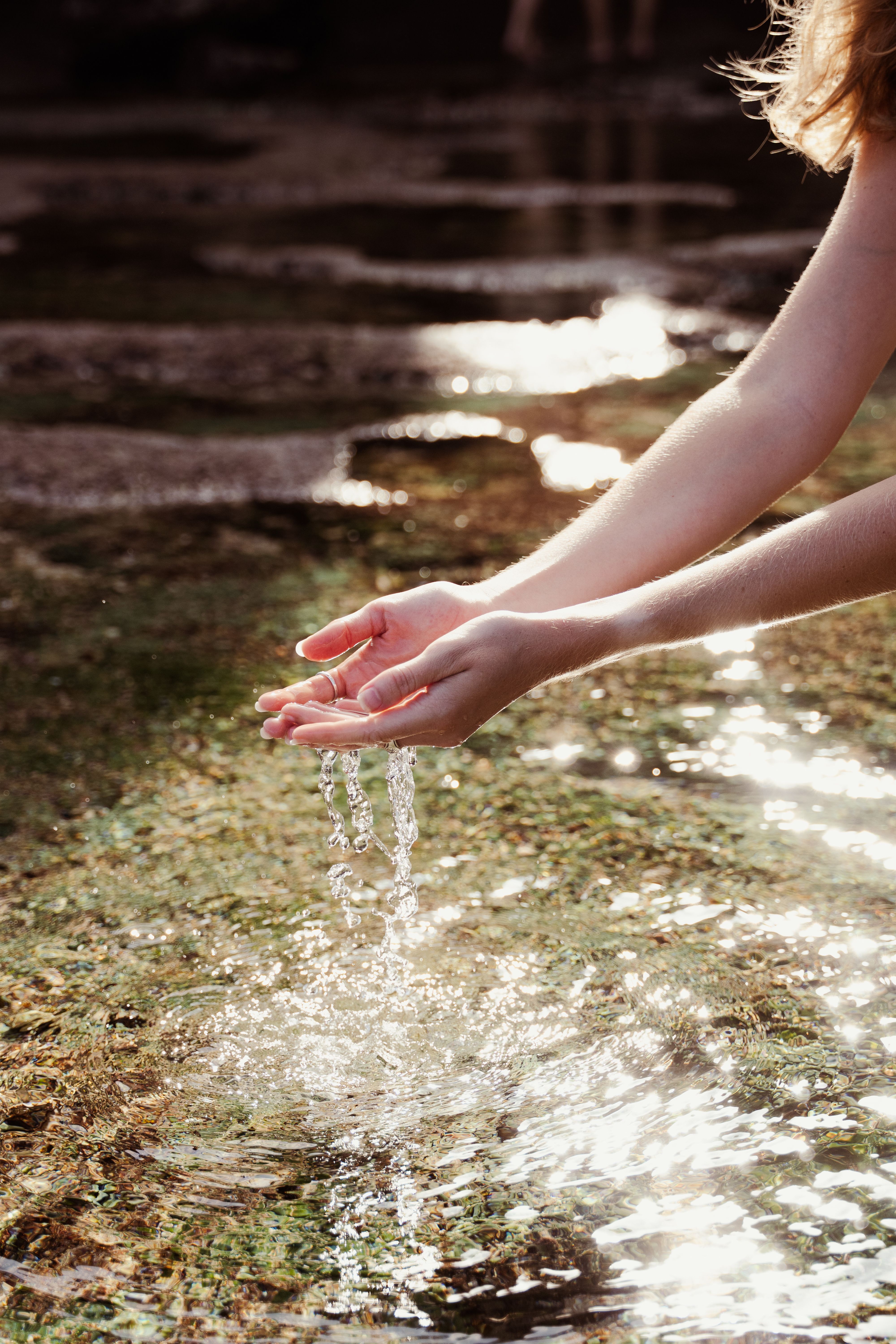 Captivating moment of hands collecting water from a sunlit stream in Bali, Indonesia.