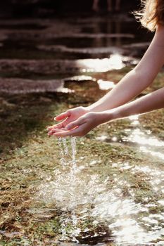 Captivating moment of hands collecting water from a sunlit stream in Bali, Indonesia.
