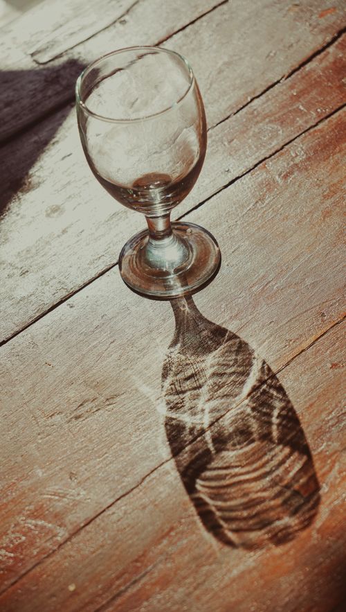 Free An artistic shot of a glass creating a detailed shadow on a rustic wooden table in sunlight. Stock Photo