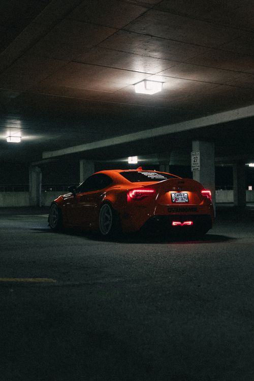 Free A striking red sports car parked in a dimly lit urban parking garage, showcasing its modern design under artificial lights. Stock Photo