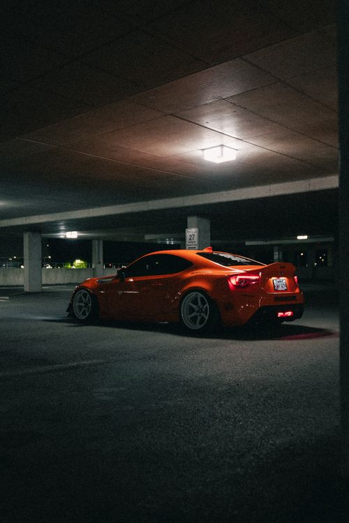 Free A sleek orange sports car parked in a moody, dimly lit parking garage at night. Stock Photo