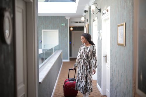 Free A woman walks with luggage through a stylish hotel corridor, embodying travel elegance. Stock Photo