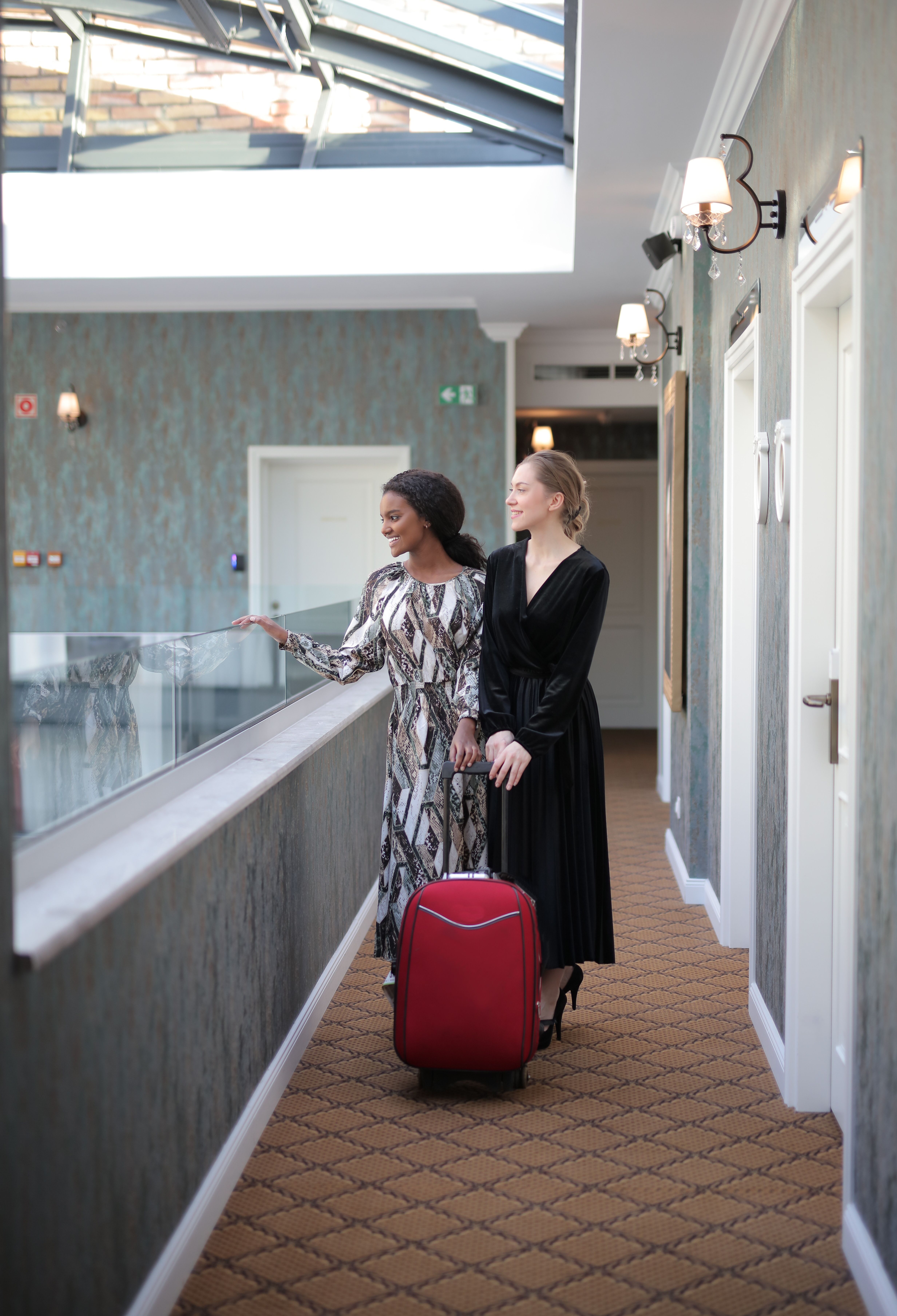 Two women in dresses with a red suitcase, stylish travel outfit inspiration