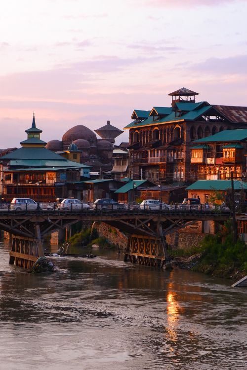 Free Picturesque sunset view of a historic bridge and buildings reflections on a serene river in an urban setting. Stock Photo