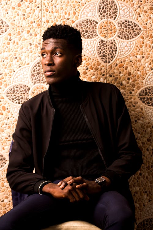 Man in Black Long Sleeve Shirt Sitting Near A Floral Design Stonewall