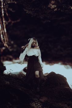 A mysterious woman holding a staff walks through a shadowy enchanted forest.