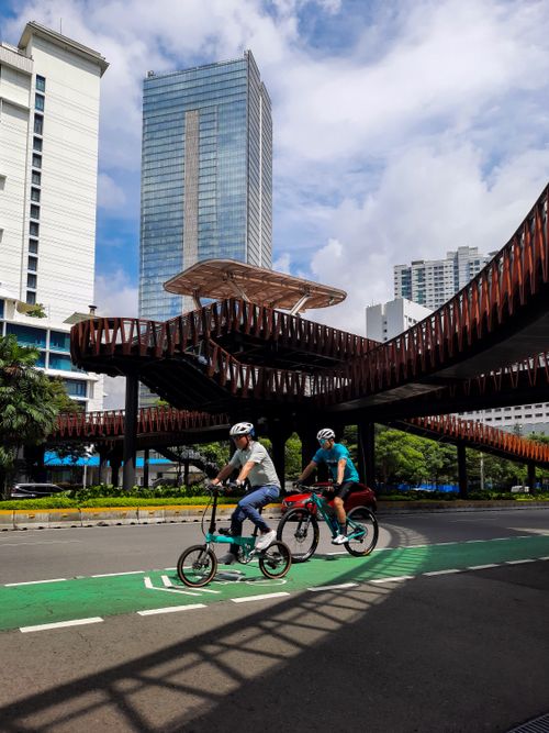 Free Two cyclists riding under a contemporary bridge in Jakarta, Indonesia, showcasing urban architecture. Stock Photo