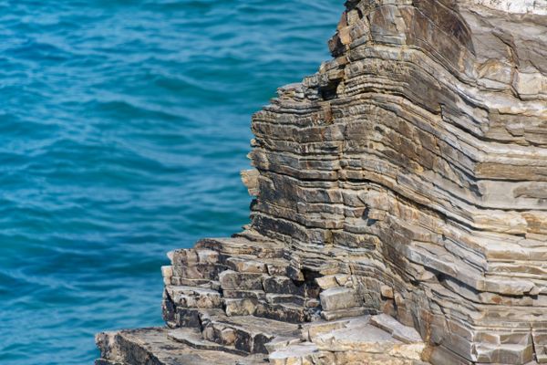 Falaise stratifiée plongeant dans une mer turquoise