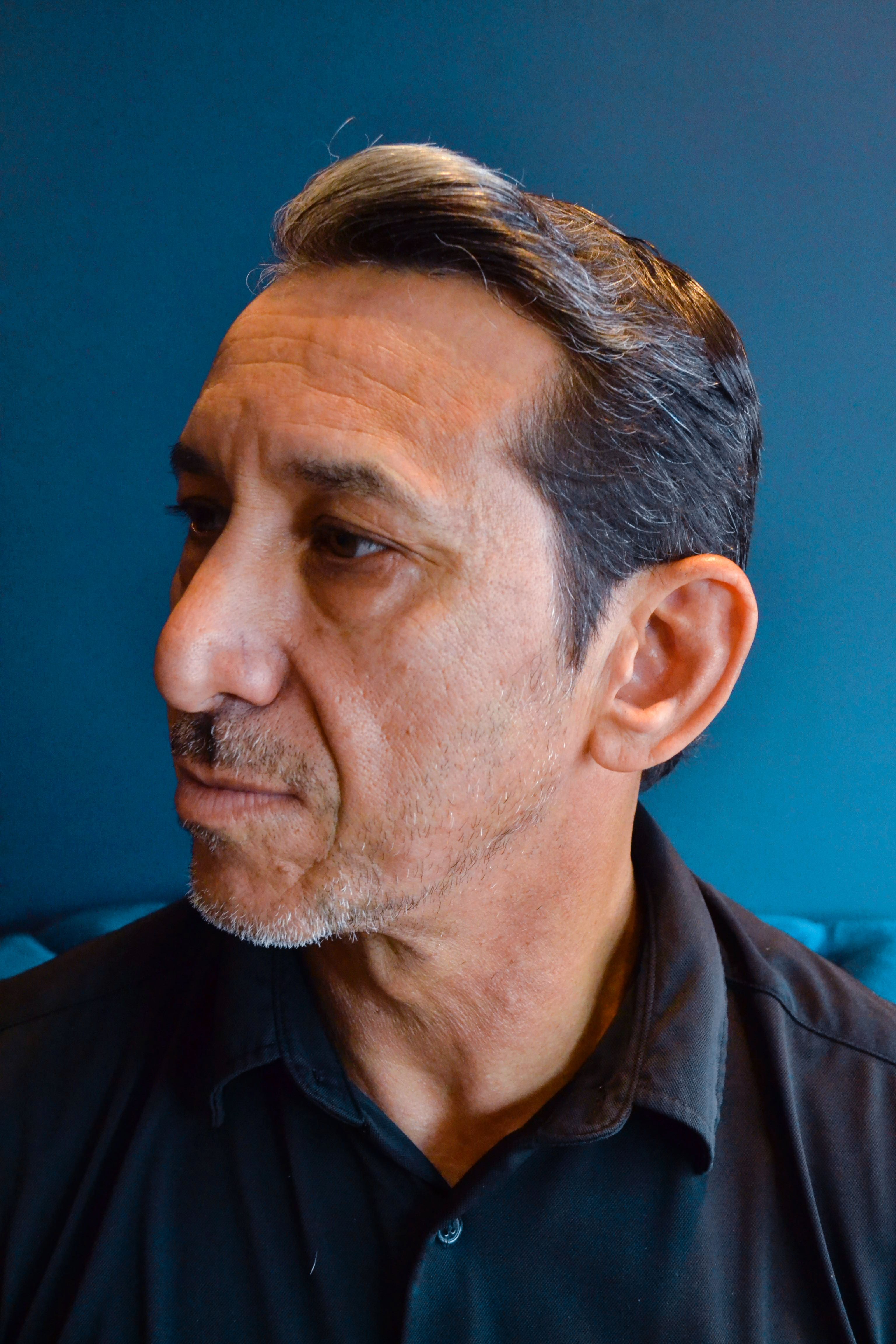 Profile portrait of a mature adult male in a blue indoor setting, headshot style.