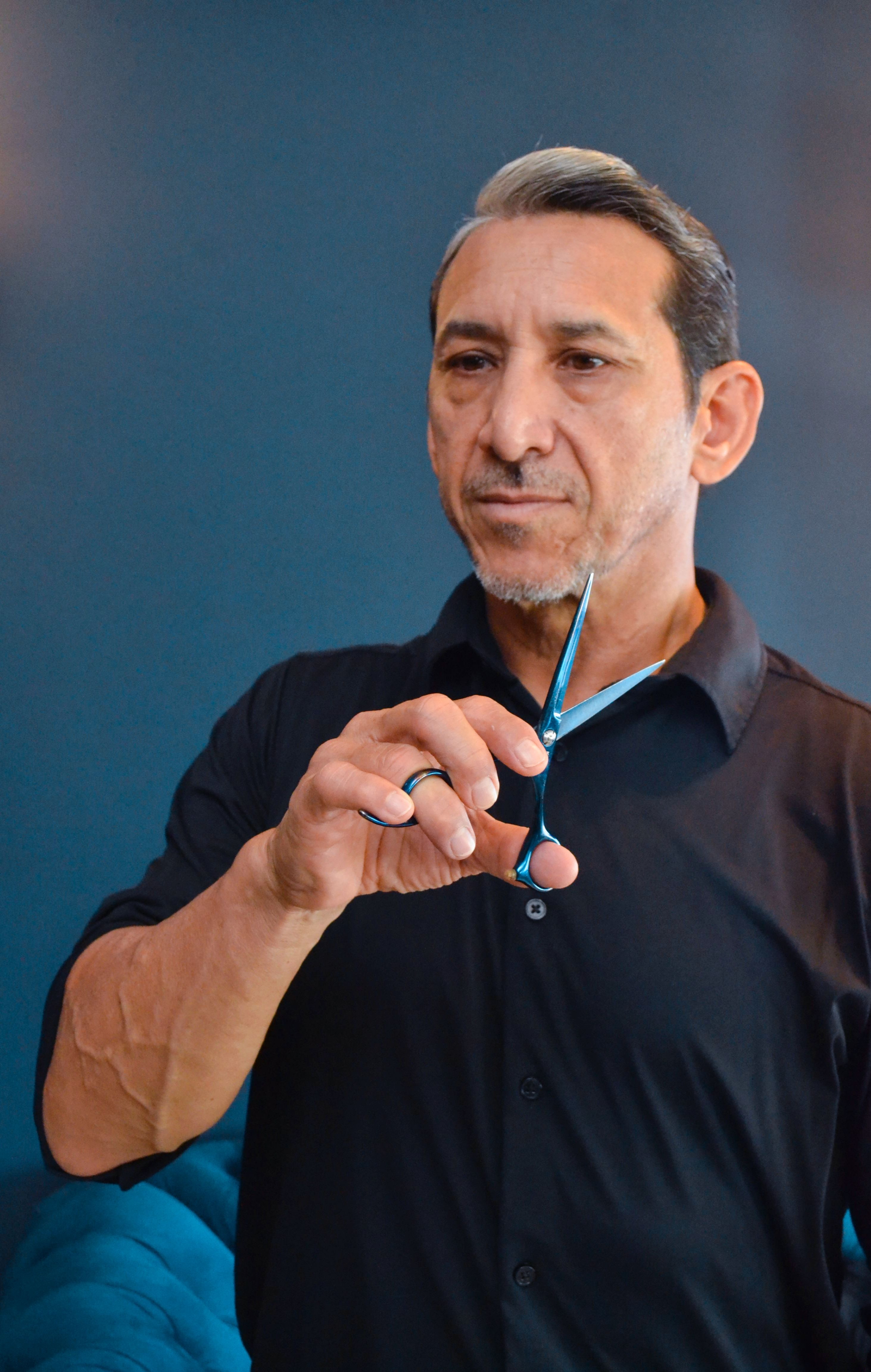 Mature male barber holding scissors ready for haircut in a modern salon.