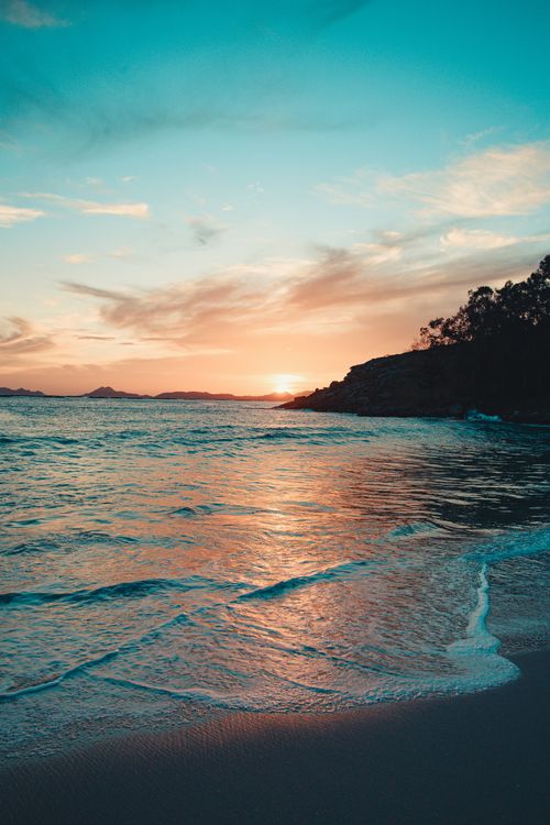 Free Calm ocean waves meet the sandy shore under a vivid sunset sky, creating a tranquil seascape. Stock Photo
