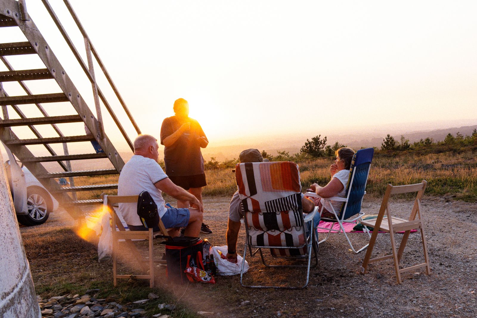 Des amis admirent un coucher de soleil doré depuis des chaises de camping, au sommet d'une colline