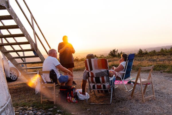 Des amis admirent un coucher de soleil doré depuis des chaises de camping, au sommet d'une colline