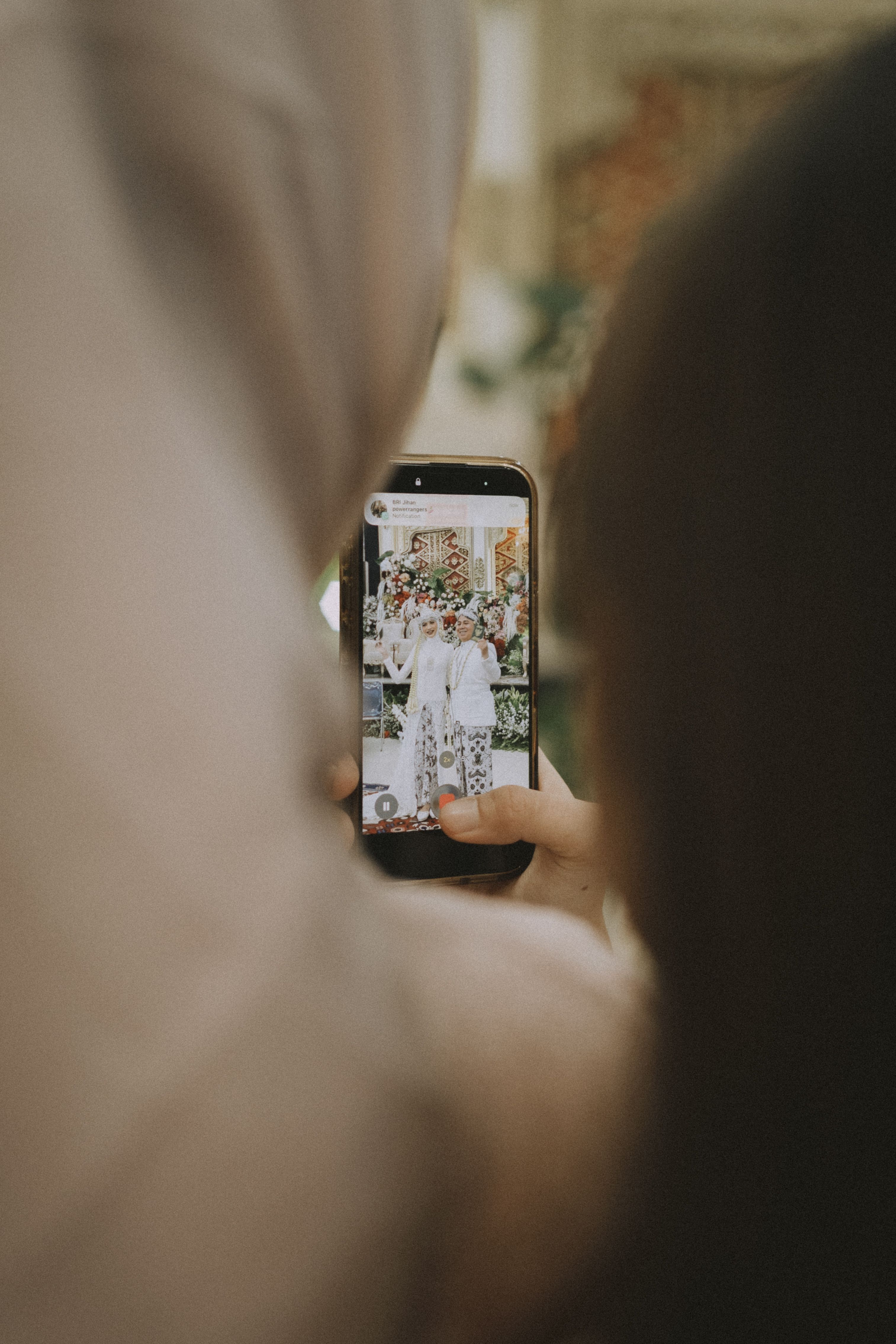 A person photographing a newlywed couple with a smartphone at an outdoor wedding