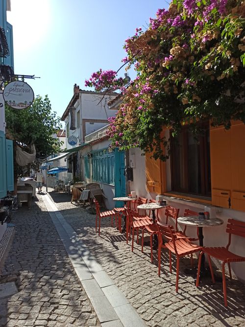 Free Sunny cobblestone street with colorful cafe chairs and bougainvillea in a Mediterranean village. Stock Photo