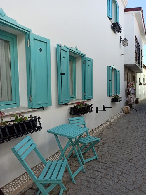 Free Quaint alleyway with turquoise shuttered windows and cobblestone path, evoking Mediterranean charm. Stock Photo