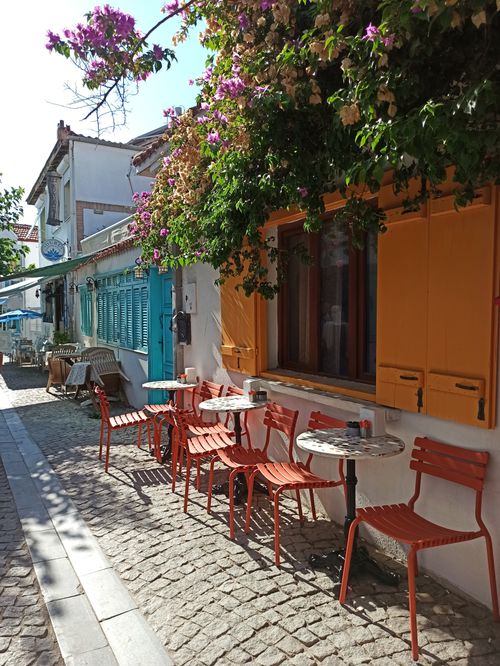 Free Outdoor cafe with vibrant chairs and lush flowers in a sunny Mediterranean village. Stock Photo