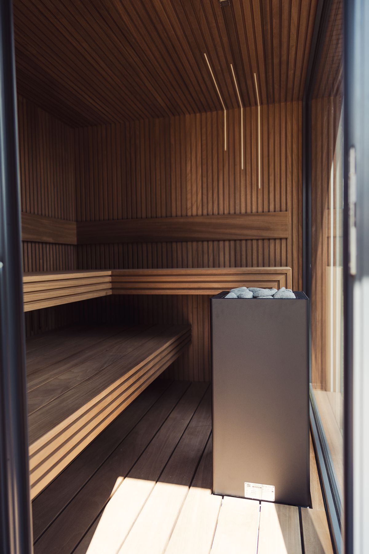 A cedar-lined sauna with slatted benches and a stone heater, daylight on the floor