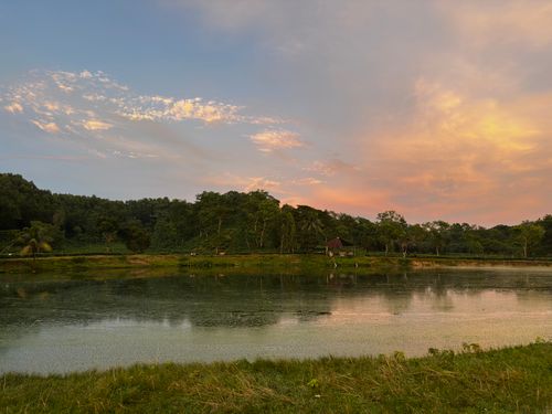 Free Serene lake with lush greenery and colorful sunset sky, reflecting calmness and natural beauty. Stock Photo