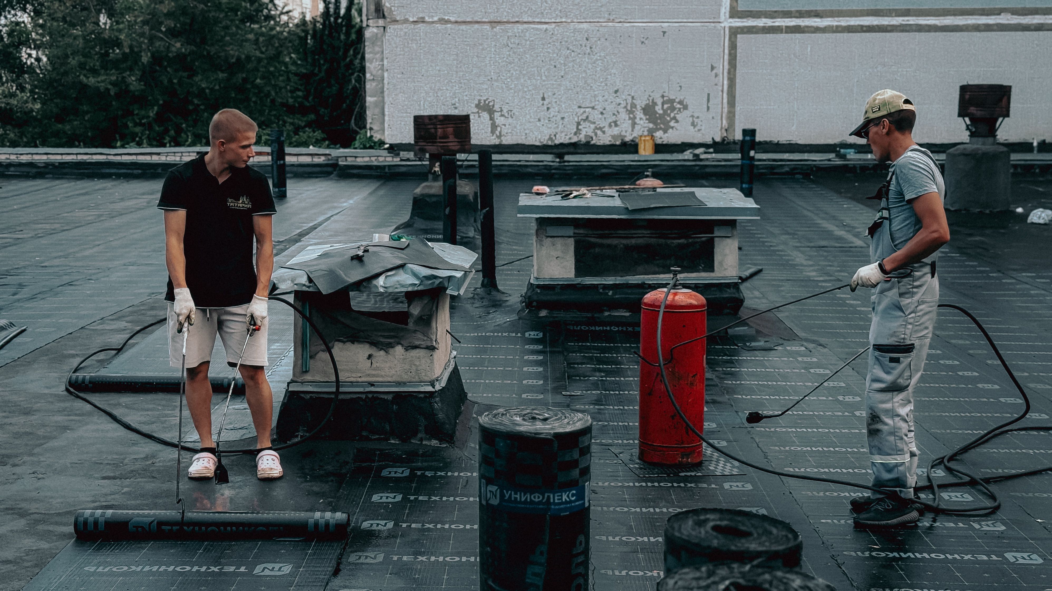 Two construction workers installing a roof insulation layer using specialized tools
