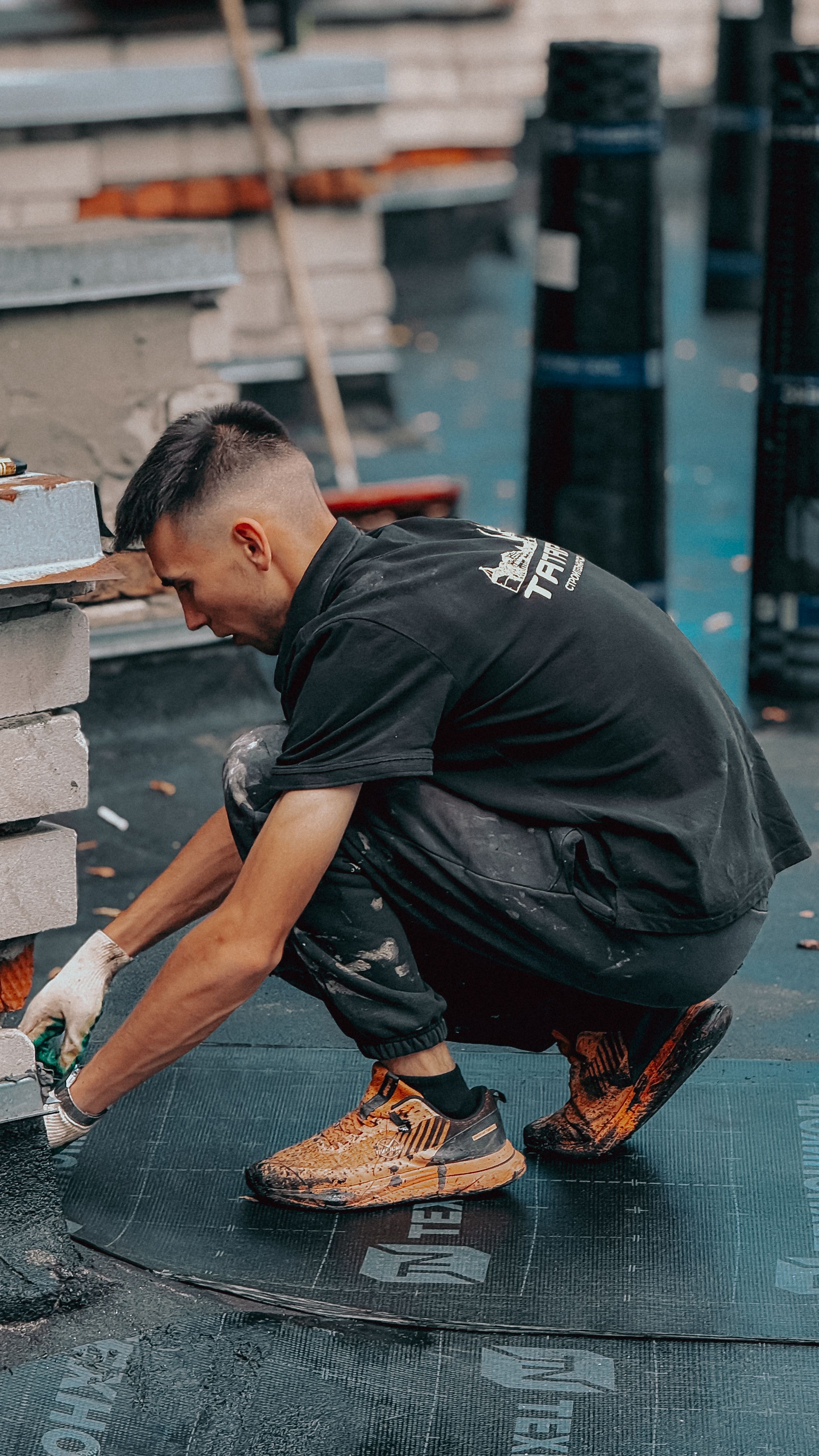 A young male construction worker focuses on installing roof tiles at a building site.