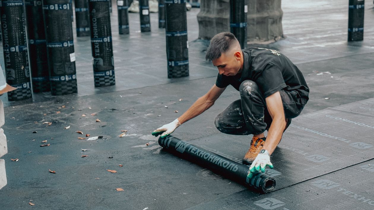 Worker applying a waterproof membrane to a flat roof on a clear day