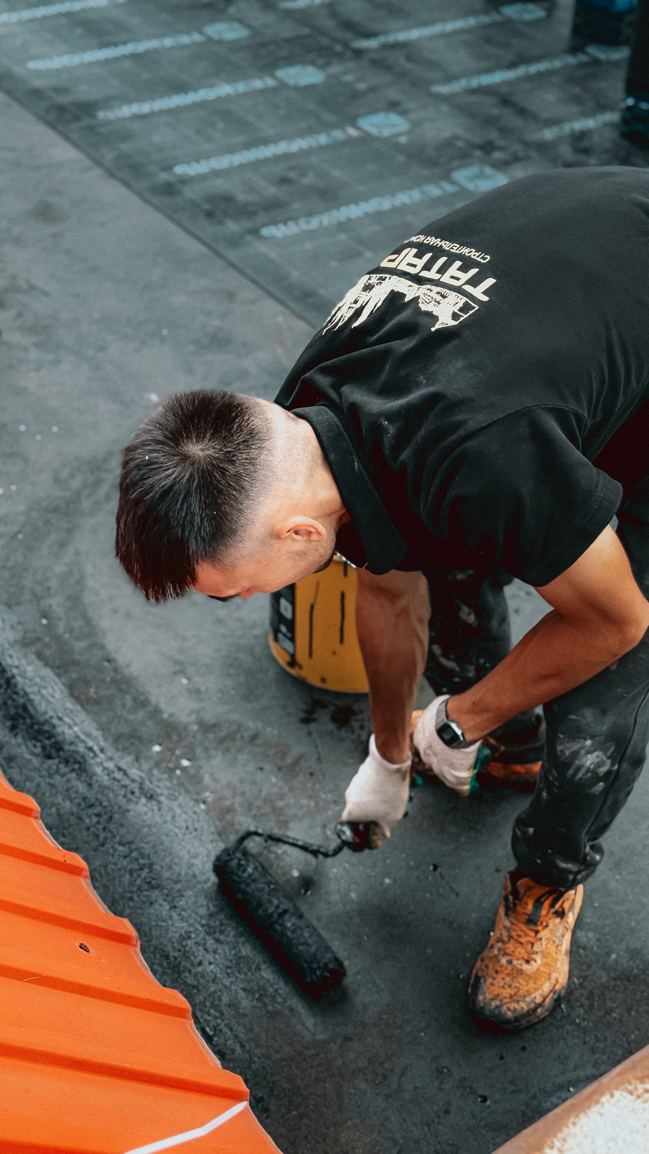 Construction worker using a roller to apply paint on roofing surface, showcasing skilled labor.