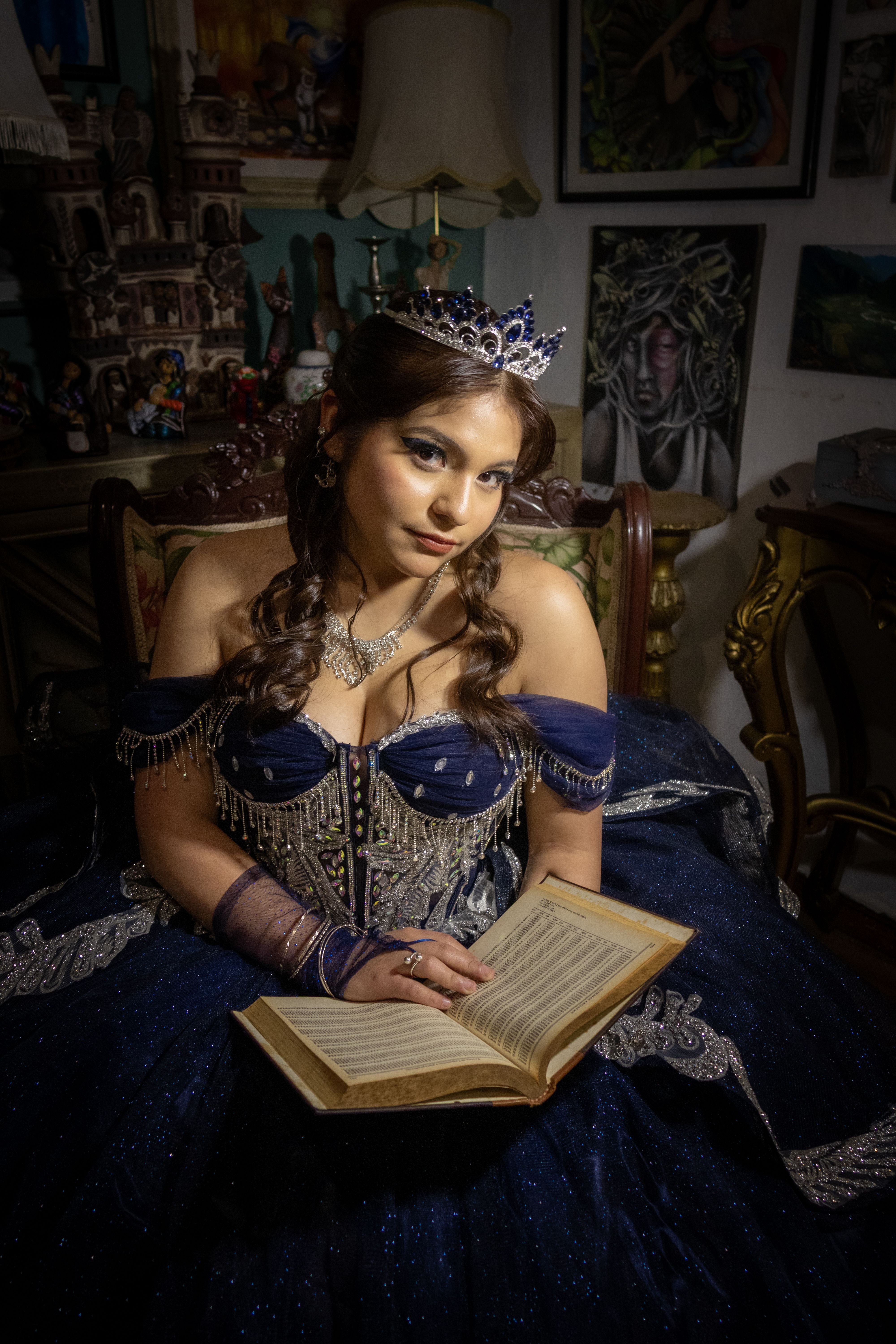 A woman dressed in a royal gown with a tiara reads an open book in an opulent room, exuding elegance and regality.