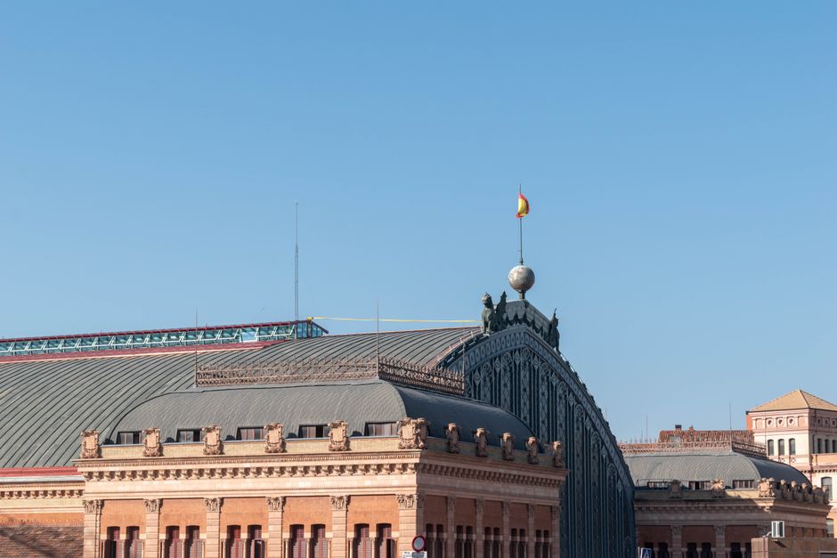 Primer plano de la emblemática estación de tren de Atocha en Madrid, donde se aprecian detalles arquitectónicos bajo un cielo azul despejado.