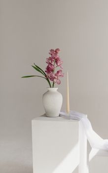 Aesthetic display of pink orchids in a white vase with a taper candle, exuding simplicity and elegance.
