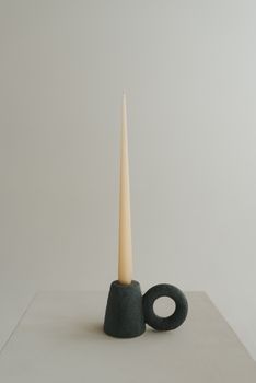 Elegant tall taper candle in a unique ceramic holder against a neutral background, showcasing minimalist design.