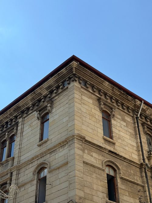 Free Wide-angle view of a historic stone building against a clear blue sky, showcasing architectural detail. Stock Photo