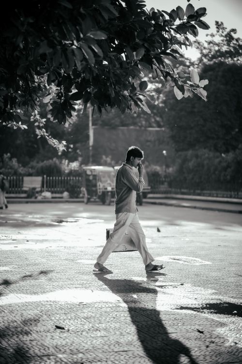 Free A man walking in a city street captured in black and white during daylight. Stock Photo
