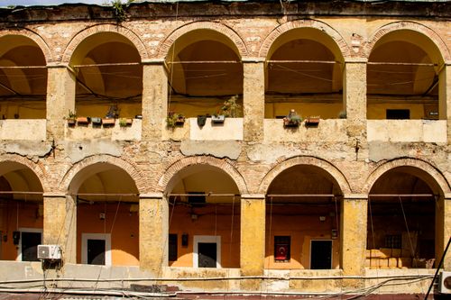 Free Sunlit facade of a historic building with stone arches and potted plants, showcasing architectural elegance. Stock Photo
