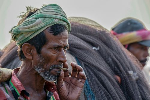Free Close-up of a fisherman contemplating life by the ocean, with nets in the background. Stock Photo