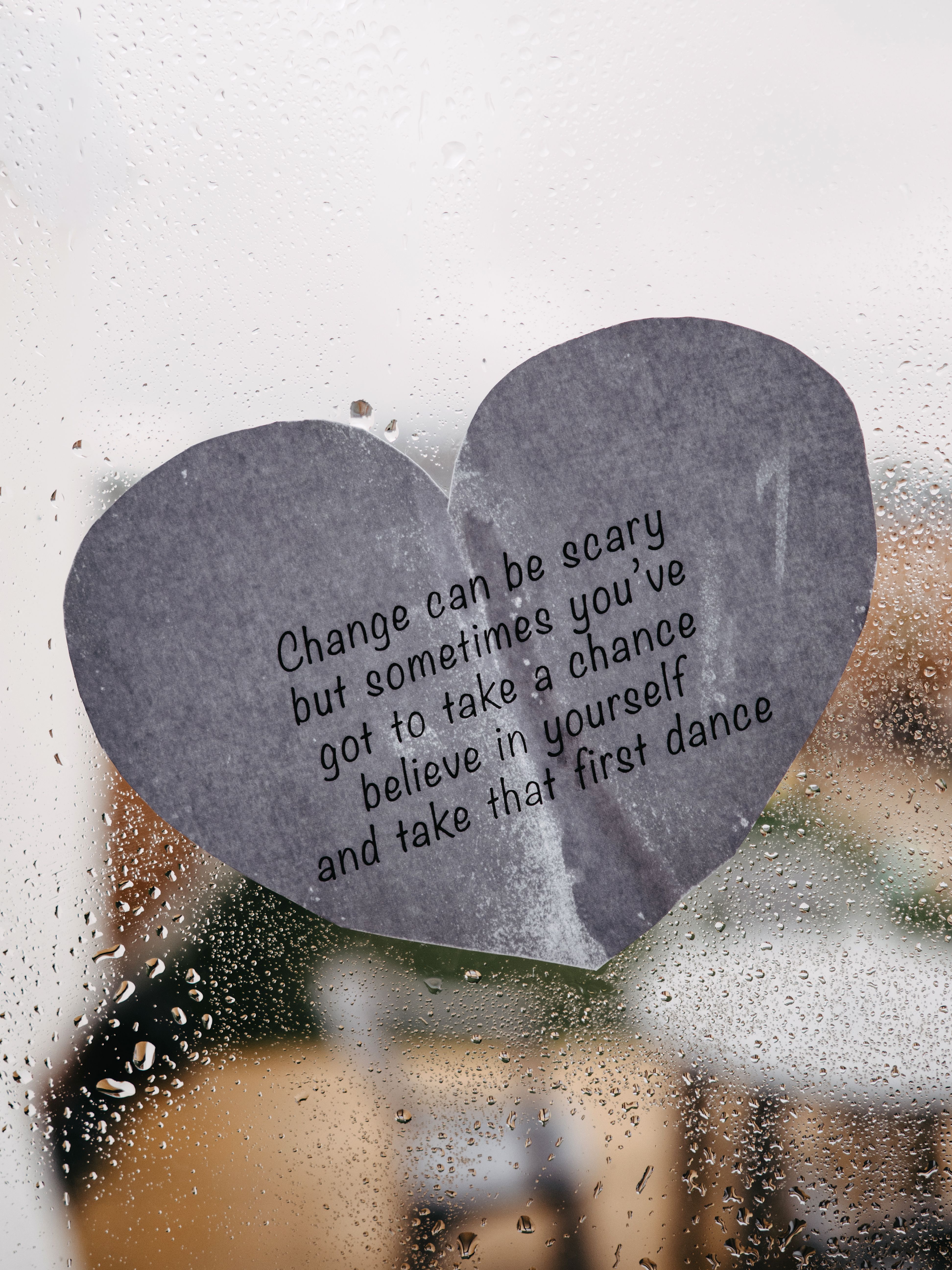 Heart-shaped paper with motivational quote against a rainy window backdrop.