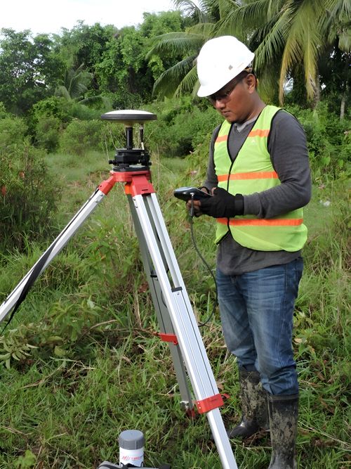 Free Surveyor using GPS equipment in a lush Indonesian landscape wearing high-visibility gear. Stock Photo