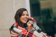 一位开朗的成年人裹着格子毯，在户外喝着啤酒，幸福感洋溢