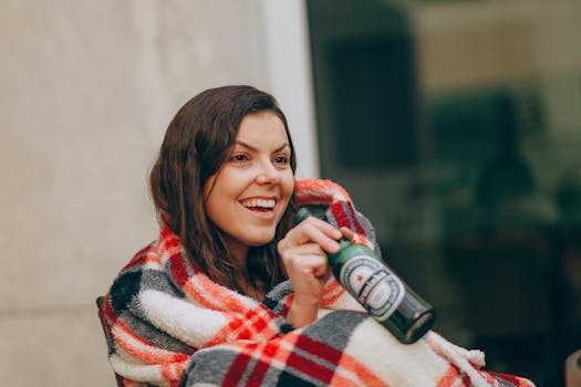 一位开朗的成年人裹着格子毯，在户外喝着啤酒，幸福感洋溢